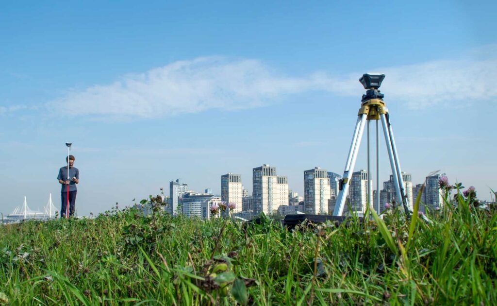 man using a survey tool on a land with a city view